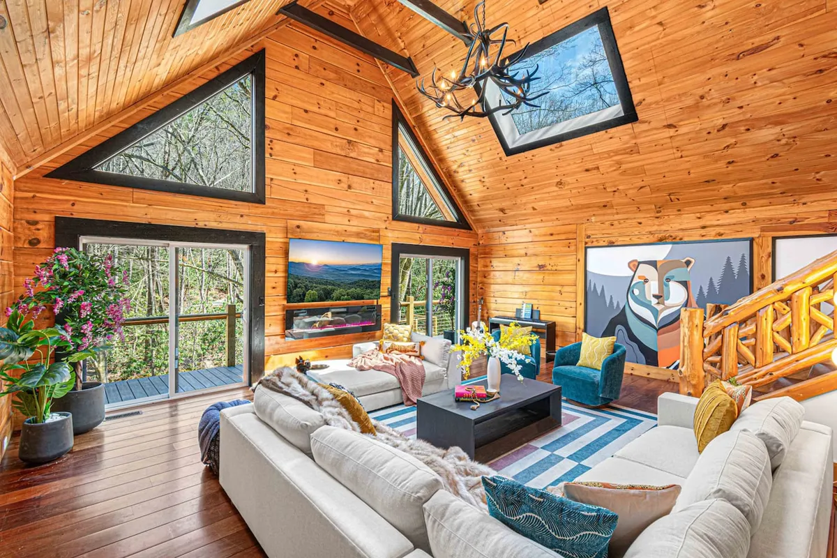 This image showcases a large, inviting sectional sofa set in a spacious living area with an artistic mural, expansive windows, and a statement chandelier. The layout encourages group gatherings and relaxation, with plenty of seating for guests to unwind together.
