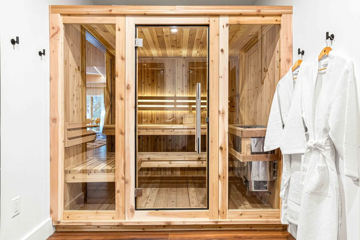 A tranquil, wood-paneled sauna with glass doors and inviting benches, set within a peaceful indoor setting. Natural light filters in, enhancing the spa-like ambiance and promising moments of solitude and restoration.