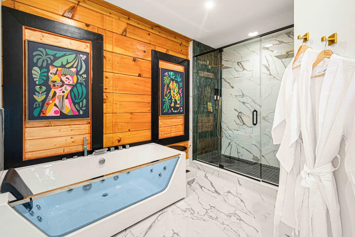 A contemporary bathroom featuring a freestanding bathtub, colorful modern artwork, a glass-enclosed shower, and warm wooden paneling. The space exudes calm, inviting long soaks and self-care rituals.
