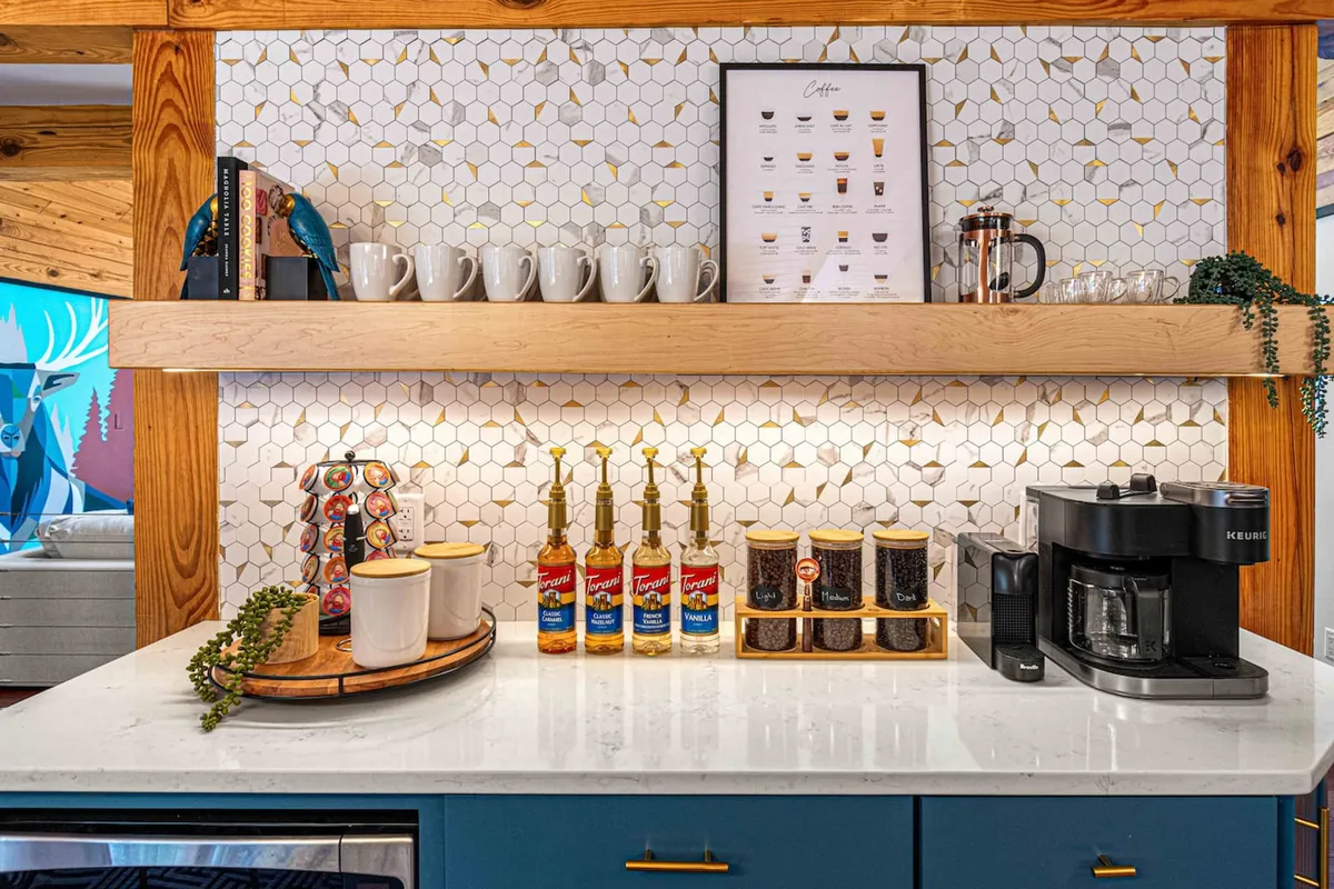 A cozy nook dedicated to coffee and refreshments, featuring a coffee machine, syrup bottles, and mugs neatly arranged on a decorative shelf. The space feels intimate and welcoming, perfect for casual morning or late-night gatherings.